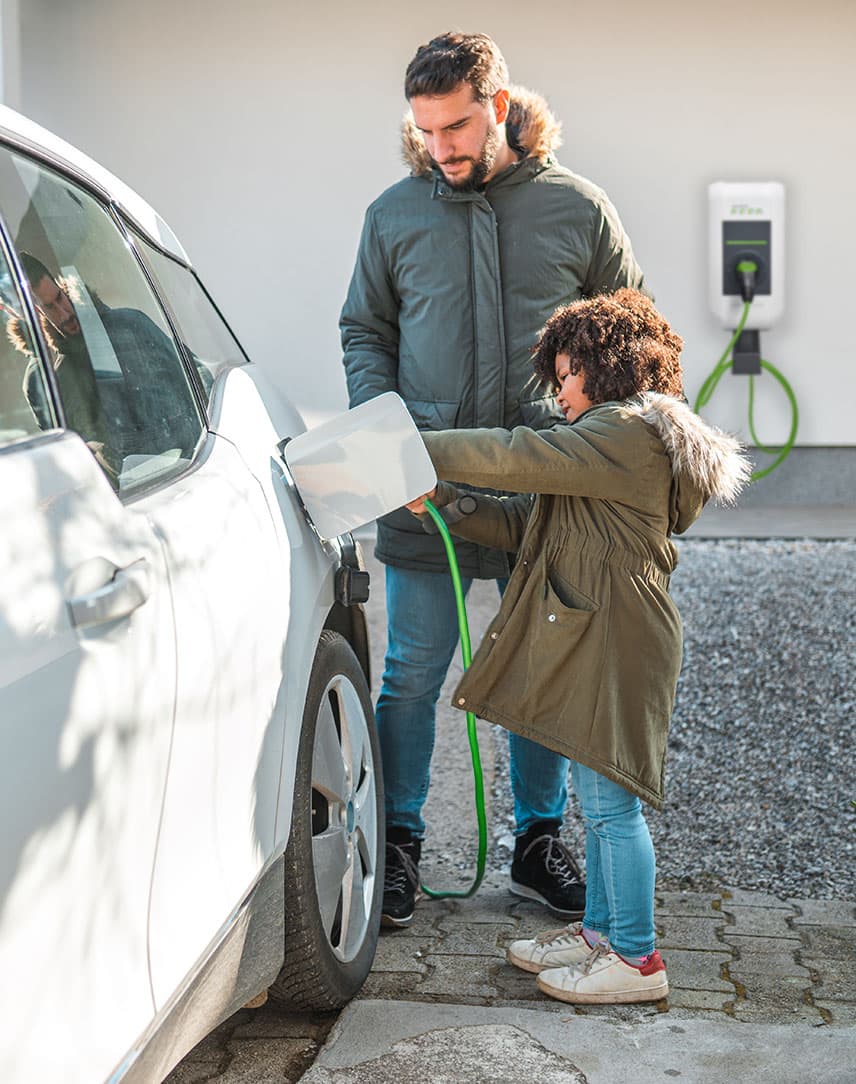 Vater und Sohn stecken den Stecker einer Wallbox in ihr E-Auto.