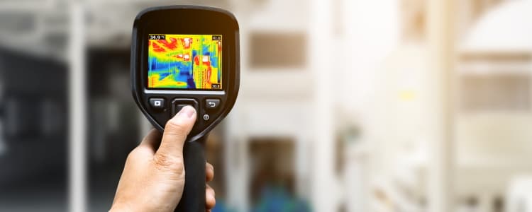 Handwerker mit Thermographie-Gerät vor einem Gebäude