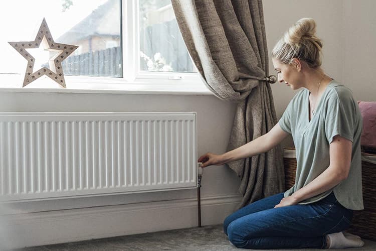 Frau dreht am Thermostat einer Heizung