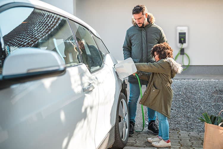 Vater und Sohn stecken den Stecker einer Wallbox in ihr E-Auto.