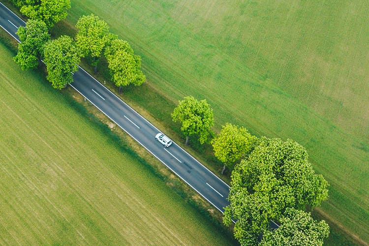 Auto auf einer Landstraße zwischen Feldern aus Vogelperspektive.