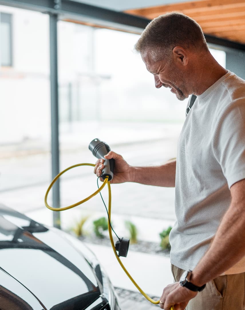Mann schließt ein Elektroauto an einer Wallbox an.