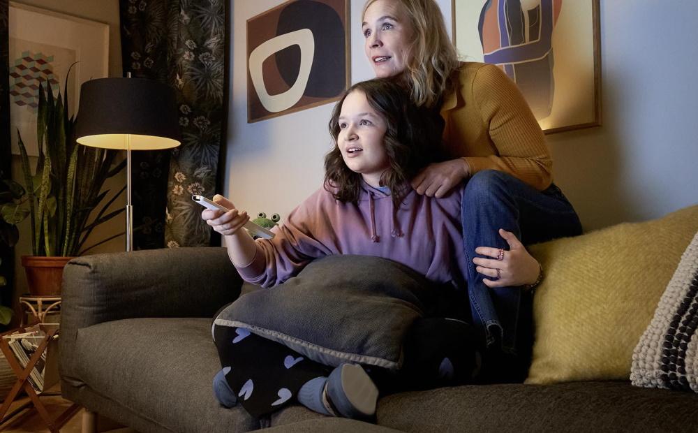 Mutter und Tochter sitzen auf der Couch mit einer Fernbedienung und schauen EWE ZuhauseTV