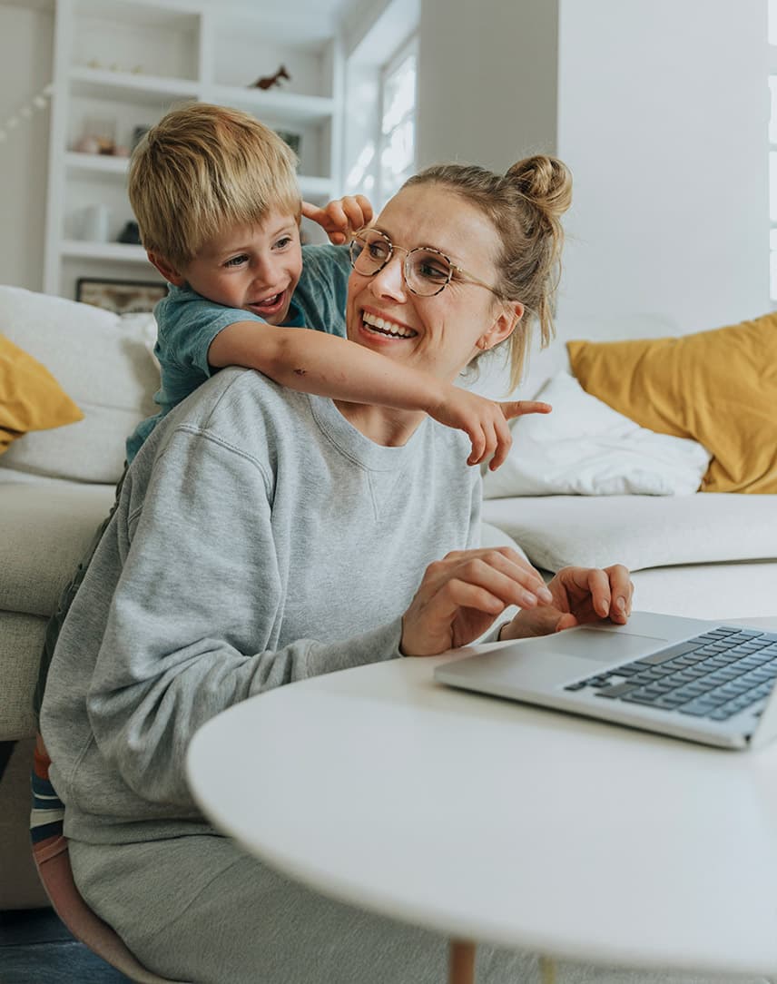 Eine Frau sitzt am Laptop, ihr Sohn umarmt sie und zeigt auf den Bildschirm