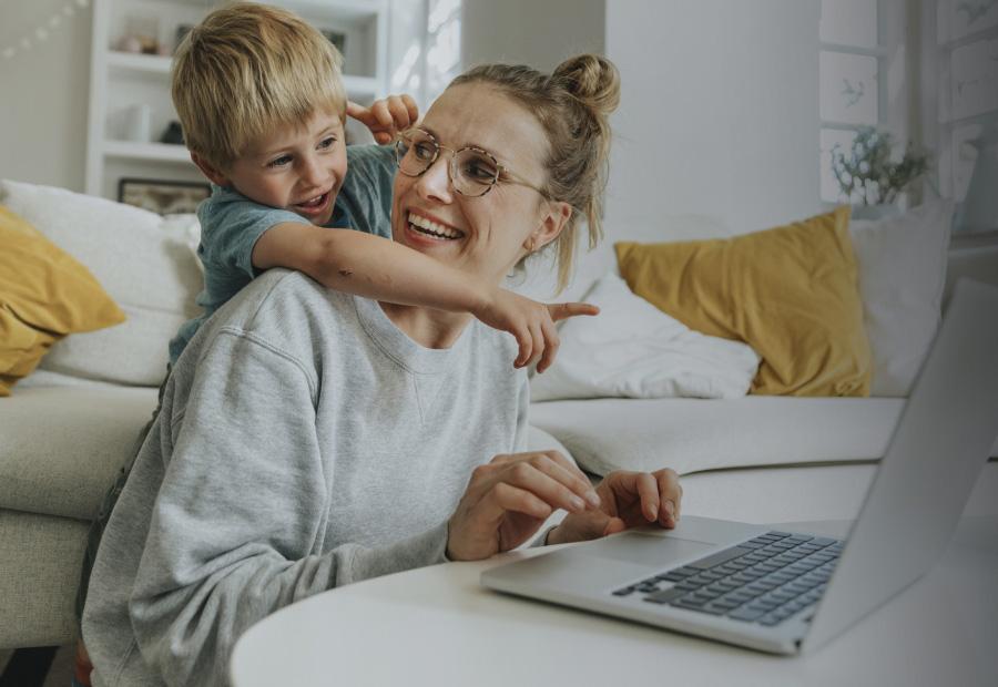 Eine Frau sitzt am Laptop, ihr Sohn umarmt sie und zeigt auf den Bildschirm