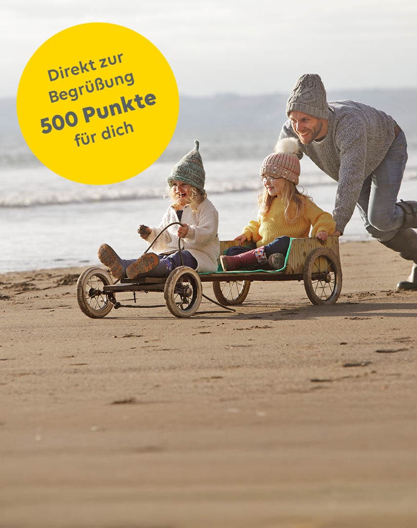 Mann schiebt zwei Mädchen in einem Wagen am Strand