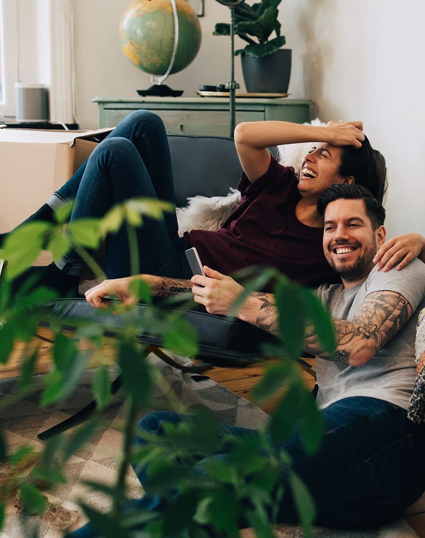 Junges Paar freut sich inmitten von Umzugskartons über den Einzug in sein neues Zuhause