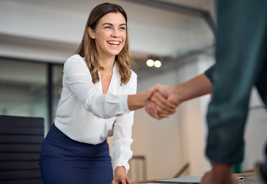 Frau begrüßt einen Kunden lächelnd per Handschlag