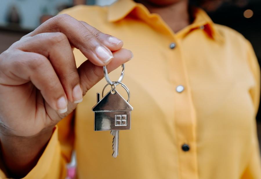 Frau hält einen Schlüssel mit einem Zuhause-Schlüsselanhänger in der Hand