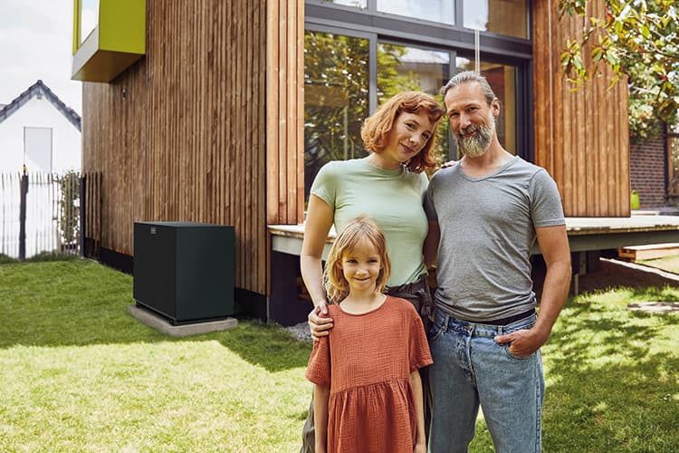 Mutter, Vater und Tochter stehen vor einem haus mit Wärmepumpe